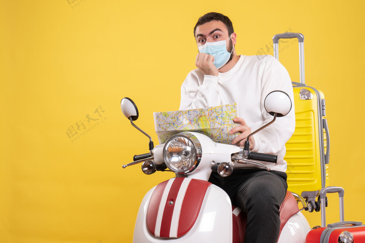 坐着旅行概念的俯视图 戴着医用面罩的困惑的家伙坐在摩托车上 黄色手提箱在上面 手里拿着地图顶视图成人
