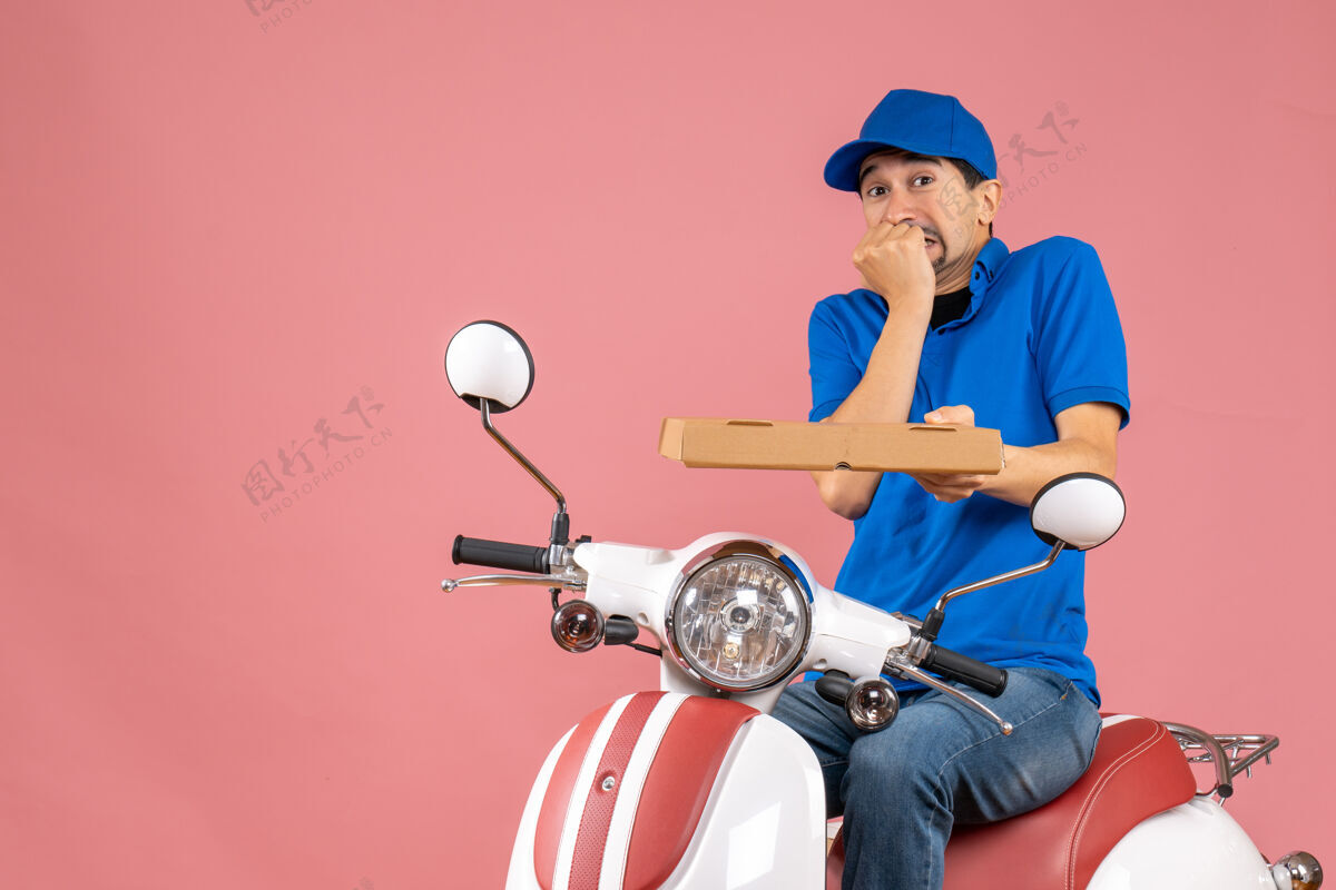 运动员前视图的信使男子戴着帽子坐在滑板车上感觉害怕粉彩桃背景摩托车桃粉彩