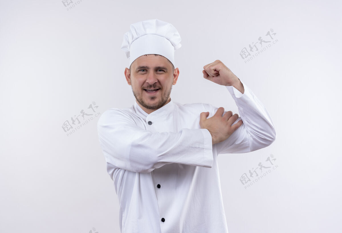 烹饪快乐的年轻帅哥厨师身着厨师制服 在白色的墙上做着强壮的手势 把手放在肩膀上英俊手手势