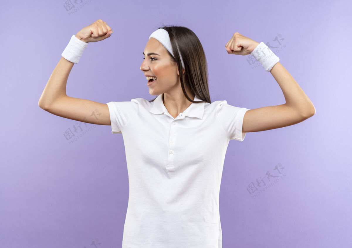 穿着快乐漂亮的运动女孩戴着头带和腕带 坚强地看着隔离在紫色墙上的一面腕带强壮漂亮