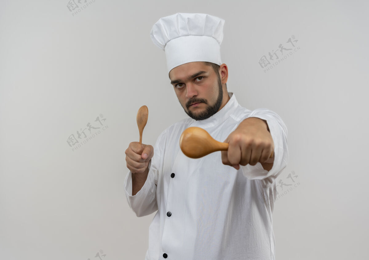 制服自信的年轻男厨师穿着厨师制服 拿着勺子 伸出勺子 孤立地放在白色的墙上 留着复印空间自信年轻厨师