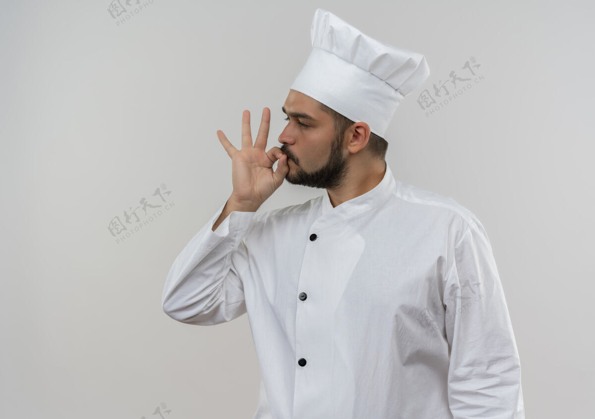 手势自信的年轻男性厨师身着厨师制服 一边看着一边做着美味的手势 一边隔离在白色的墙壁上 留着复制空间自信制服厨师