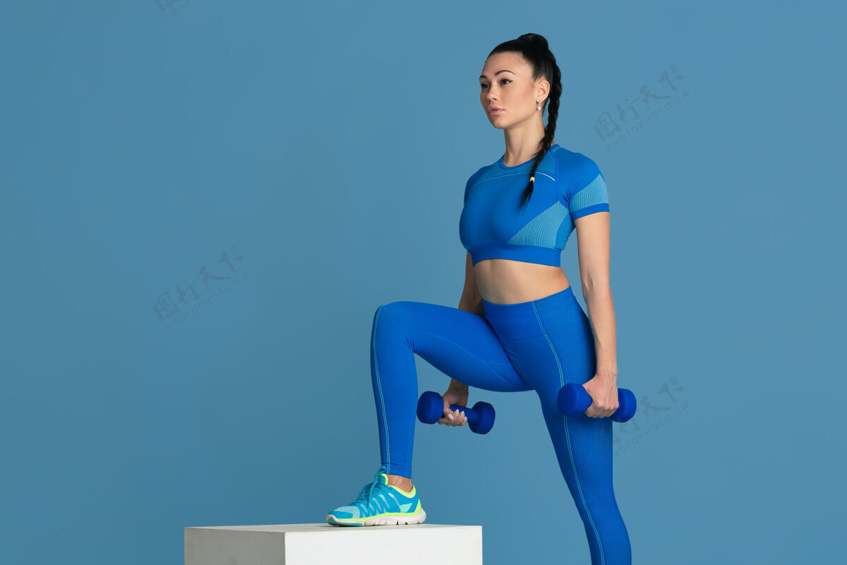 运动员踏步美丽的年轻女运动员在工作室练习 单色蓝色肖像女人身体健身房