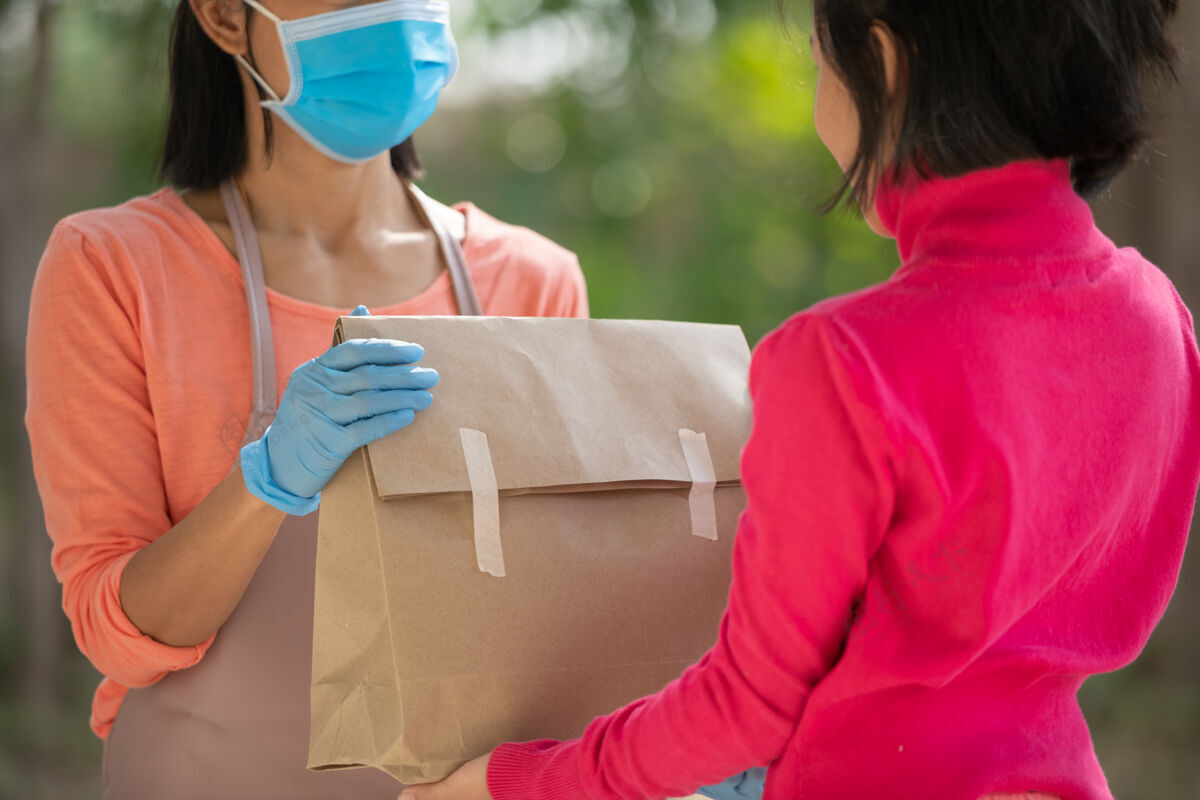 保护邮递员 送货员戴着口罩提着小盒子送到顾客家门口女士戴着口罩防止冠状病毒19型感染爆发送货上门购物理念自然快递服务