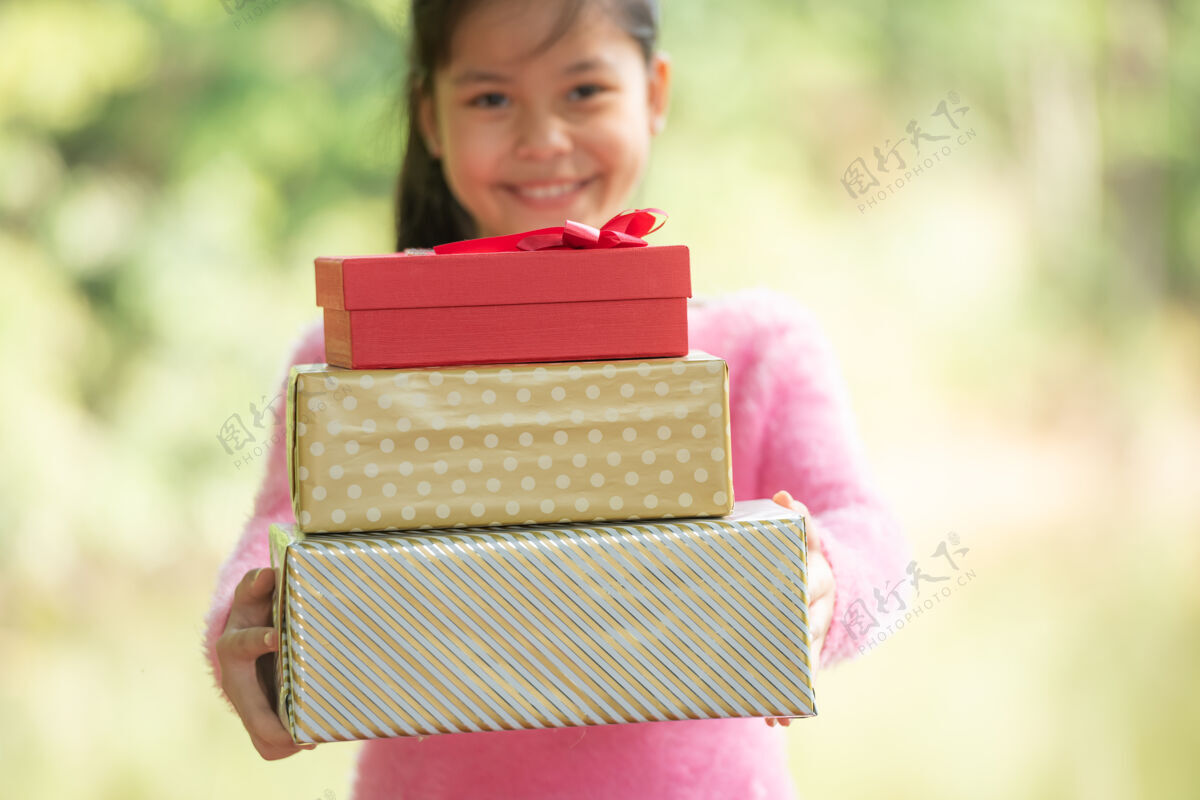 礼物圣诞快乐微笑的小女孩与礼品盒的肖像画在一棵绿色的树枝旁绿色的树叶从自然森林的背景中突出包装蝴蝶结天