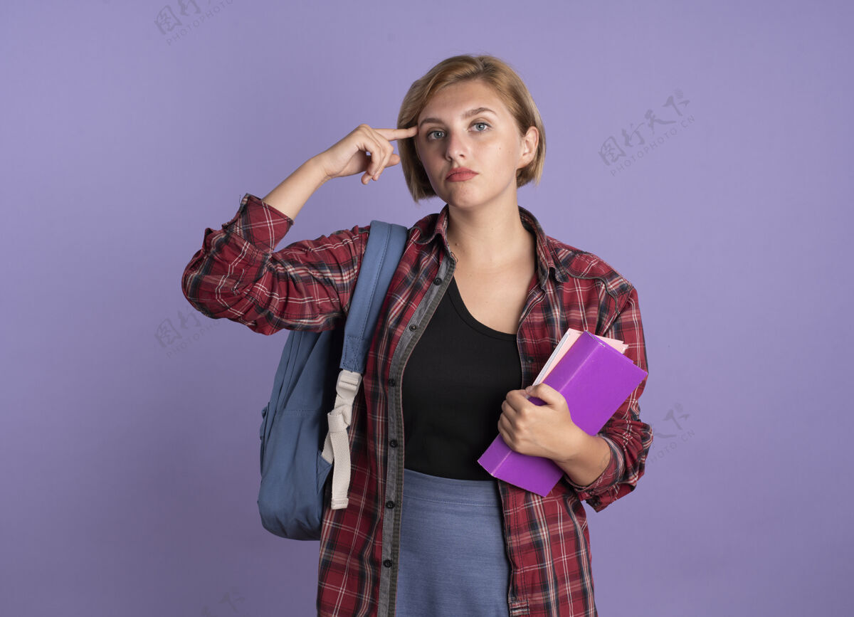 穿自信的年轻斯拉夫女学生背着背包把手指放在太阳穴上拿着书和笔记本手指空间笔记本