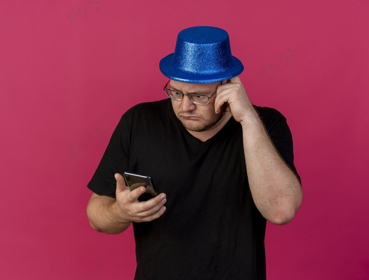持有焦急的成年斯拉夫人戴着眼镜 戴着蓝色派对帽 手里拿着电话看焦虑男士复制
