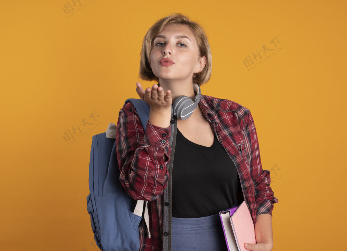 学生自信的年轻斯拉夫女学生戴着耳机背着背包 用手送吻亲吻发送复制
