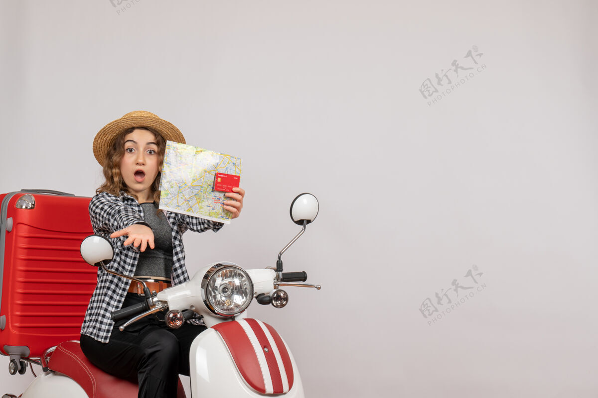 地图骑在轻便摩托车上的年轻女子拿着灰色的卡片和地图 心里很奇怪灰色摩托车时尚