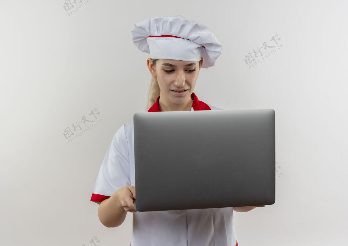 制服年轻漂亮的厨师穿着厨师制服拿着笔记本电脑 看着隔离在白色墙上的复印空间烹饪年轻厨师