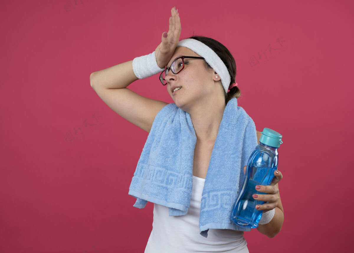 手戴着眼镜 脖子上围着毛巾 戴着头带和腕带 手里拿着水瓶 手放在额头上 惹恼了年轻的运动女孩粉红色年轻运动