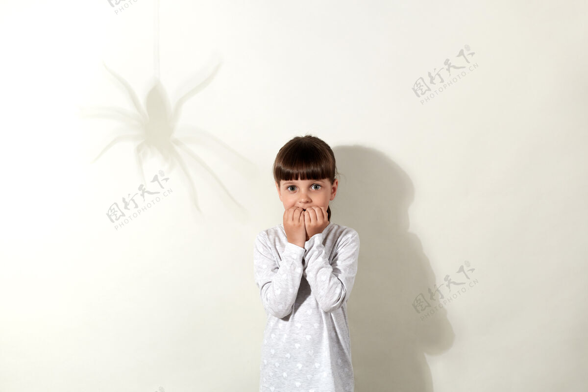 恐惧蜘蛛恐惧症一头黑发 墙上有蜘蛛的影子 吓坏了小女孩 一双吓坏了的大眼睛直视着小女孩 咬着她的指甲 穿得很随意恐惧色调害怕