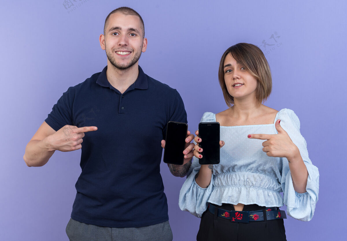 拿着一对年轻漂亮的夫妇手持智能手机 食指指着手机 微笑着 快乐而积极地站着电话积极站着