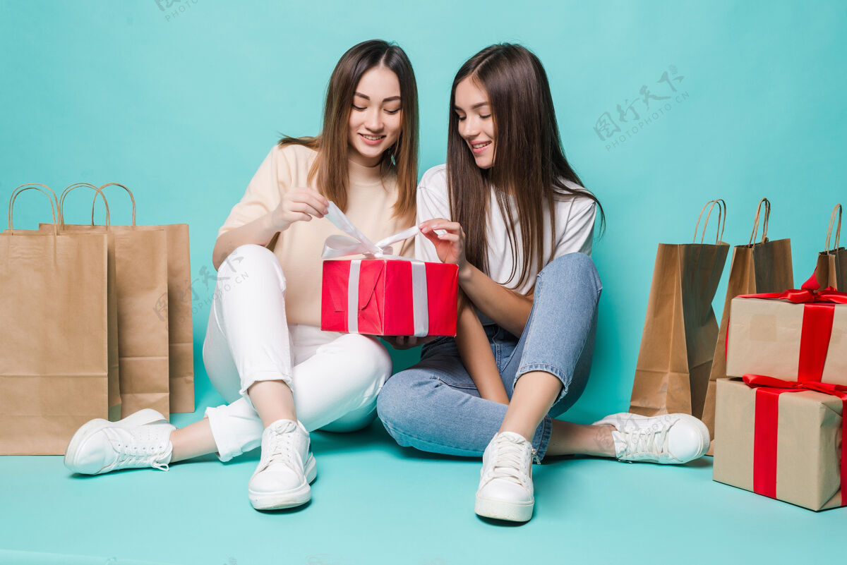 赛车微笑的年轻两个女孩坐在地板上购物袋和打开礼物的绿松石墙上惊喜衣服情感
