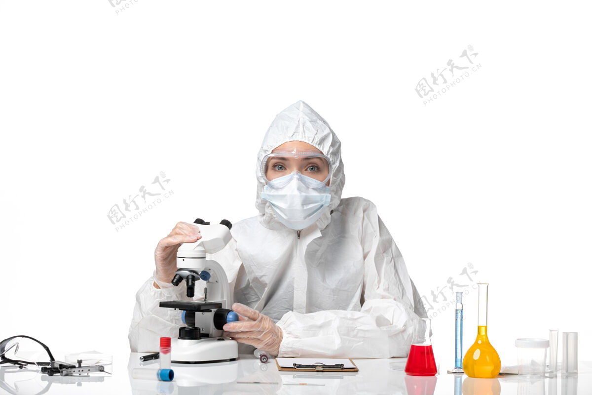 专业正面图年轻女医生穿着白色防护服 戴着口罩 由于科维德在显微镜下工作 白色背景病毒大流行飞溅科维德-工作医生显微镜