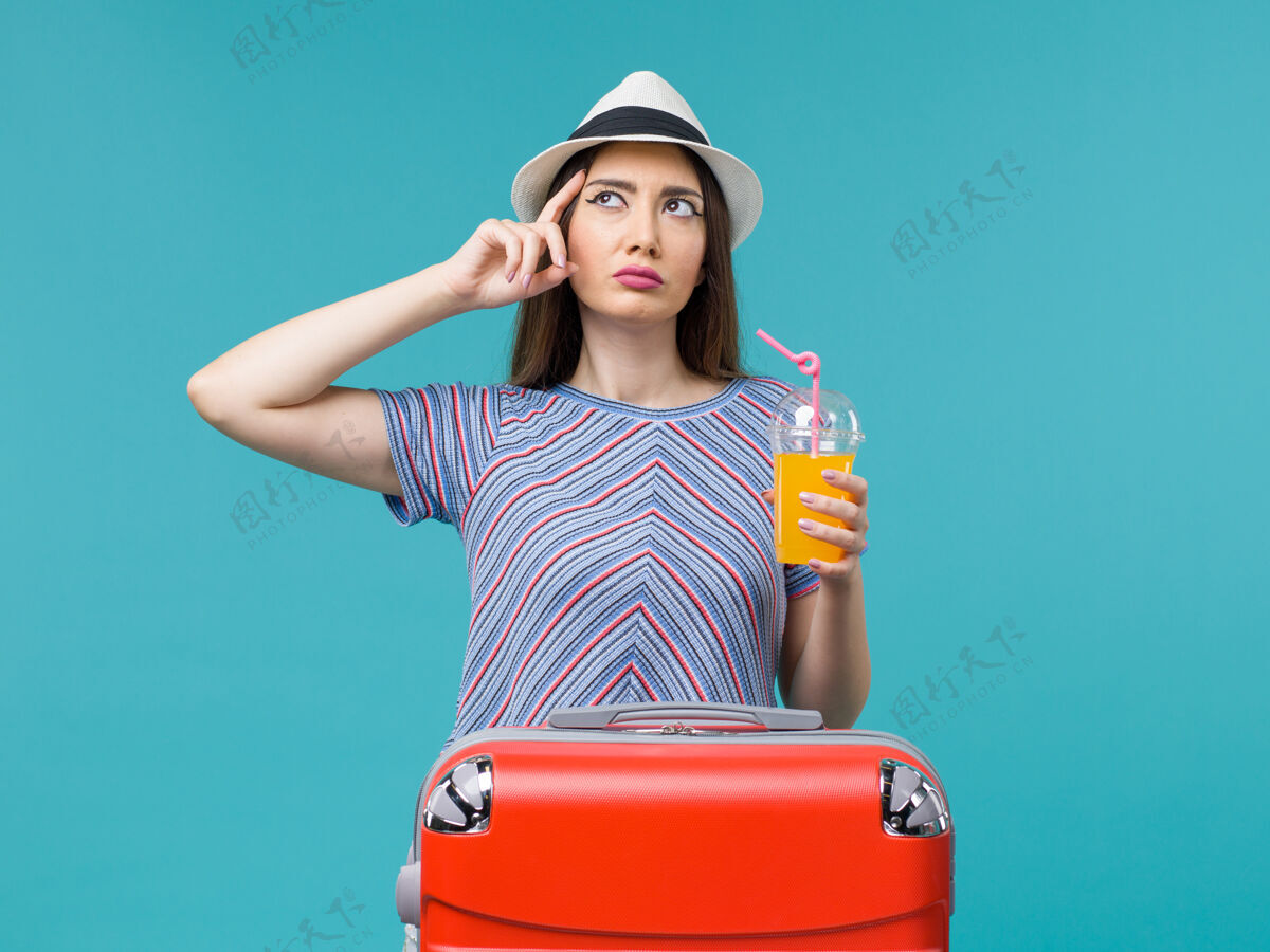 人前景度假中的女人拿着她的红色袋子 拿着她的果汁 在蓝色的背景下旅行 夏天的海上旅行旅行果汁旅程