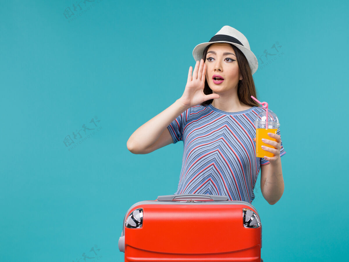 旅行前景度假的女人拿着她的红色袋子拿着她的果汁在蓝色背景上旅行度假的女人女性肖像举行