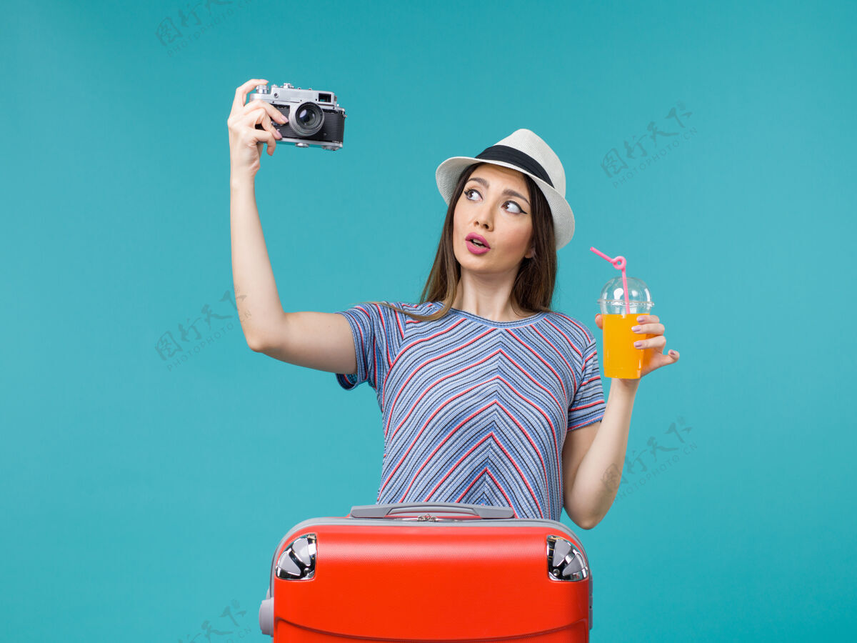 果汁前景度假中的女人拿着果汁和相机在蓝色的背景海上航行暑假美丽旅行肖像