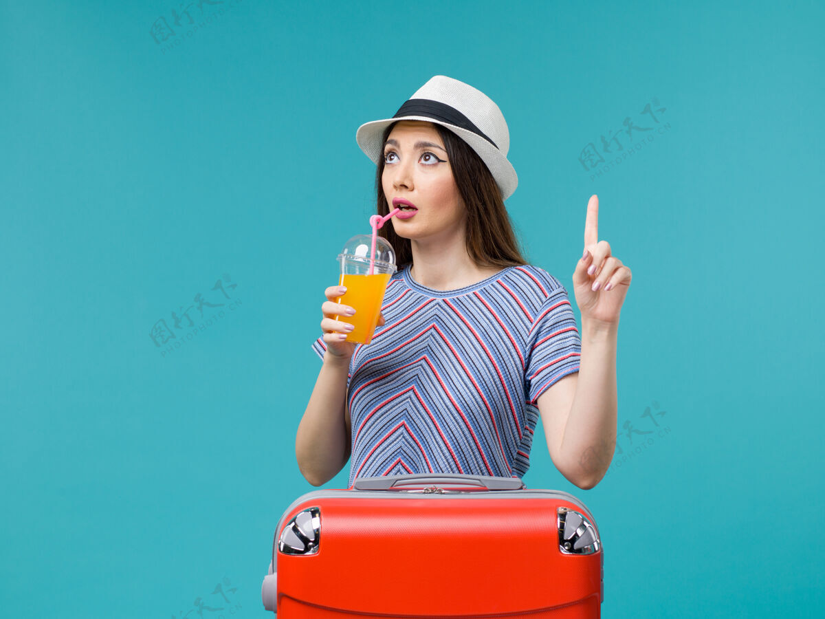 肖像前景度假中的女人带着她的红色袋子拿着她的果汁在淡蓝色的背景下旅行夏季海上旅行度假果汁旅行包