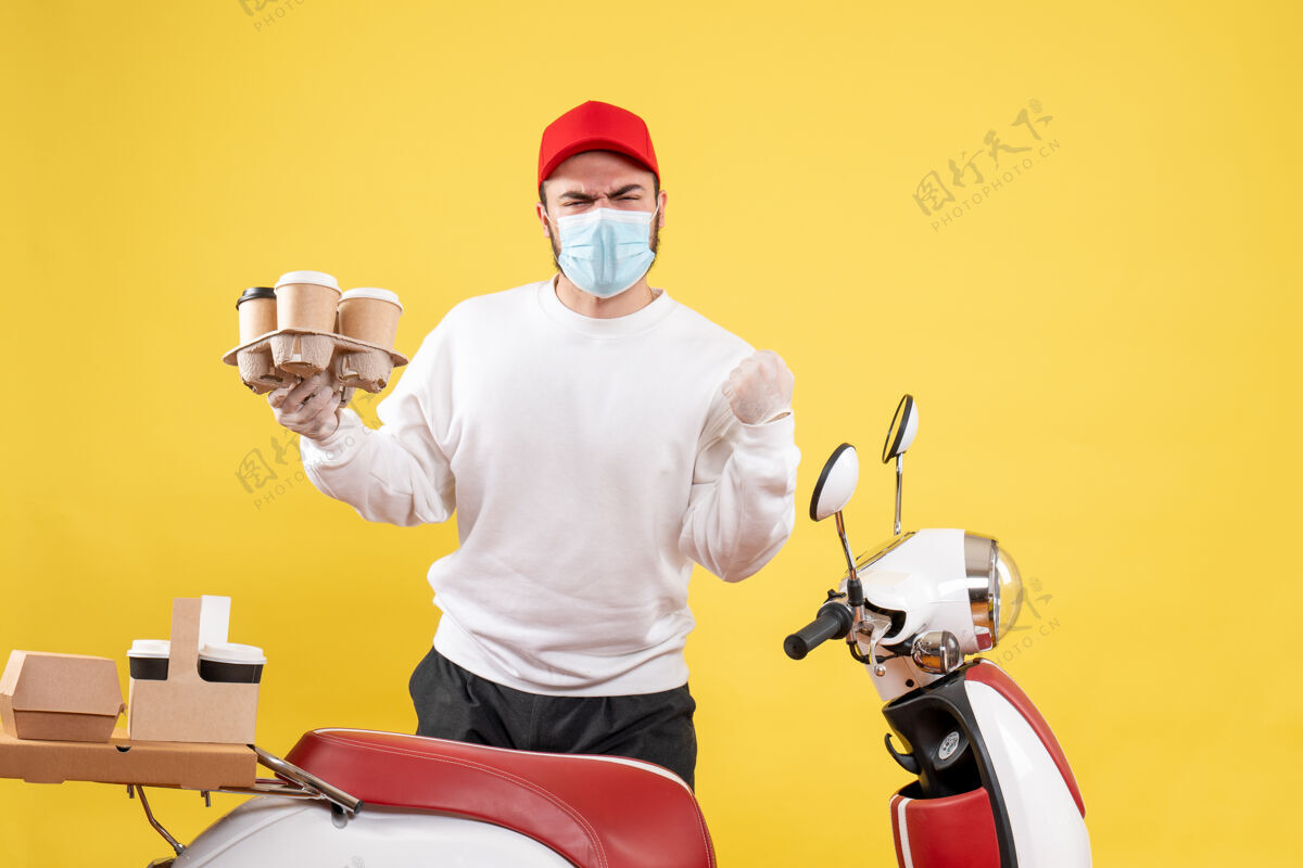 口罩戴着面具的男信使拿着黄色的咖啡送货头盔人
