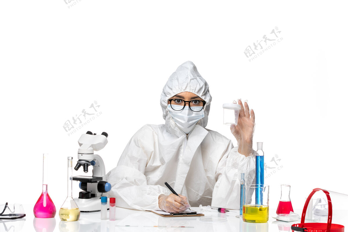 化学正面图身穿特殊防护服的年轻女化学家拿着空烧瓶 在白桌子上写着实验室病毒-化学病毒健康专业面具保护