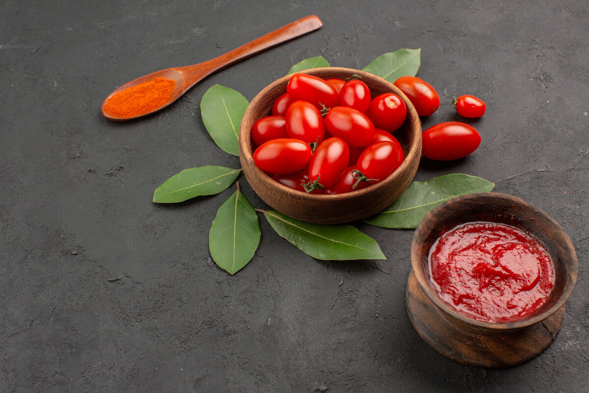 健康一碗樱桃番茄在黑色的桌子上留下一个木勺和一碗番茄酱浆果碗成熟