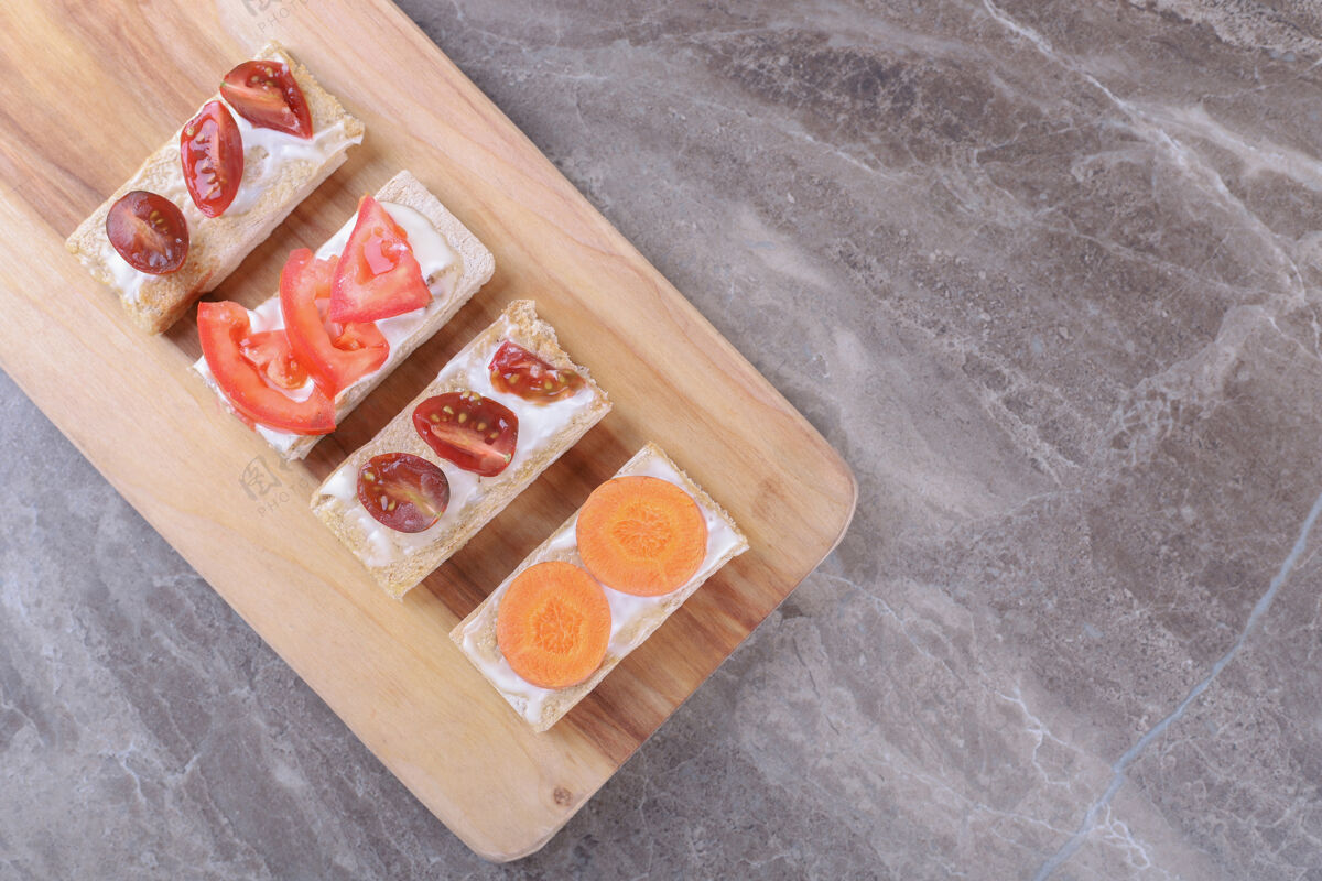 大米把胡萝卜和西红柿片放在酥脆的面包上 放在大理石表面美味风味饼干