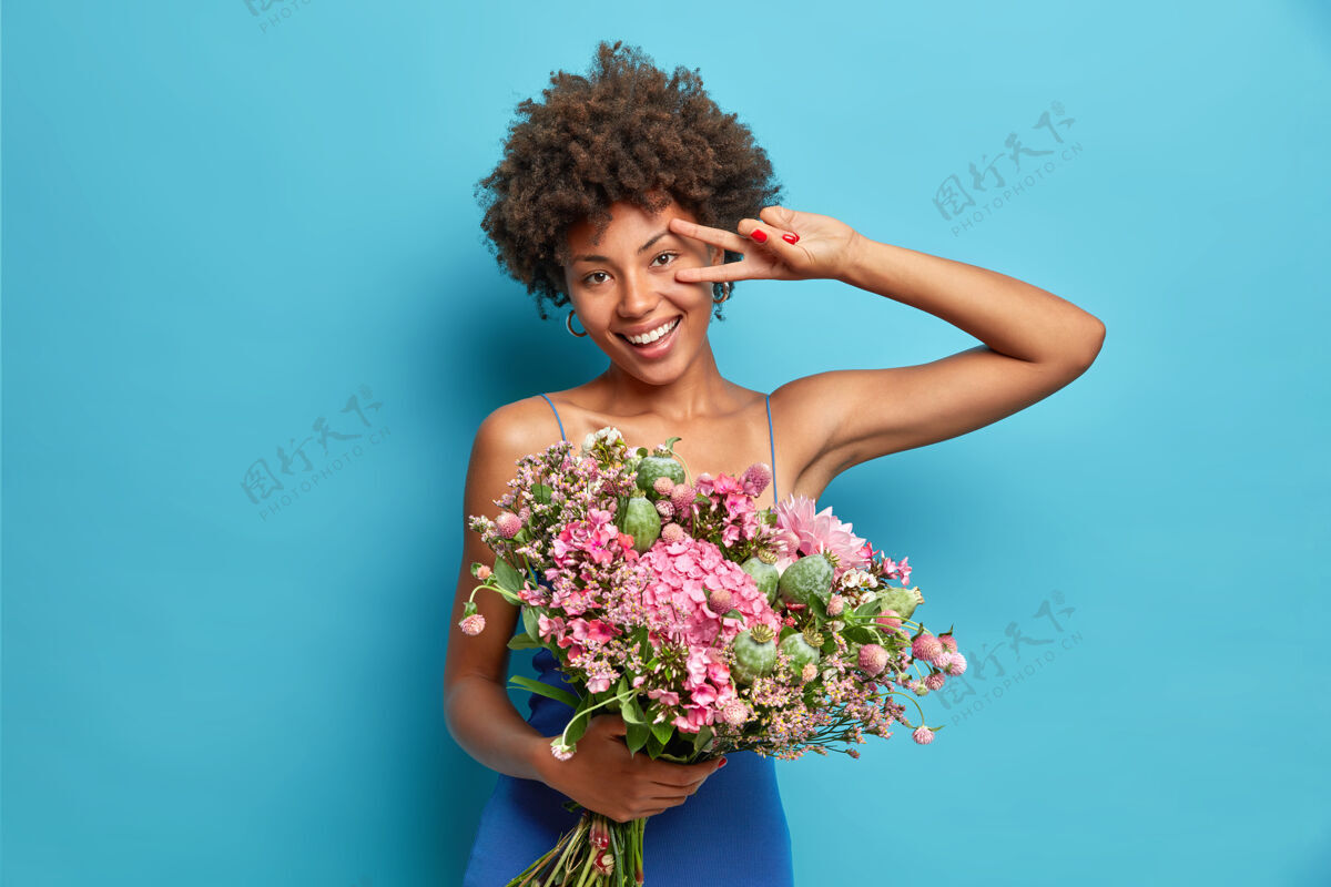 服饰开朗的年轻女子横拍展现出平和的姿态 手持大束鲜花 笑容灿烂 喜庆的心情隔着蓝色的墙壁女性胜利自然