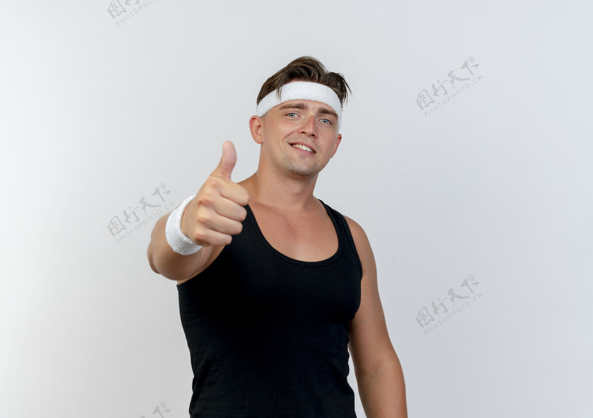表情面带微笑的年轻帅气的运动型男子戴着头带和腕带 在白色的墙壁上孤立地向前伸出大拇指帅气衣服人
