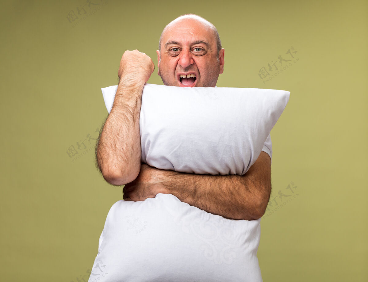 枕头恼怒的成年病高加索男子抱着枕头和保持拳头在橄榄绿的墙壁与复制空间隔离白种人拳头成人