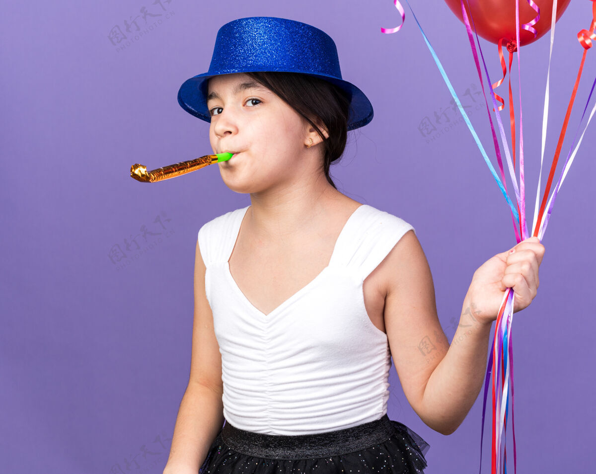 吹快乐的年轻白种人女孩 戴着蓝色派对帽 手持氦气球 吹着派对哨子 在紫色的墙壁上与复制空间隔离白种人拿着年轻