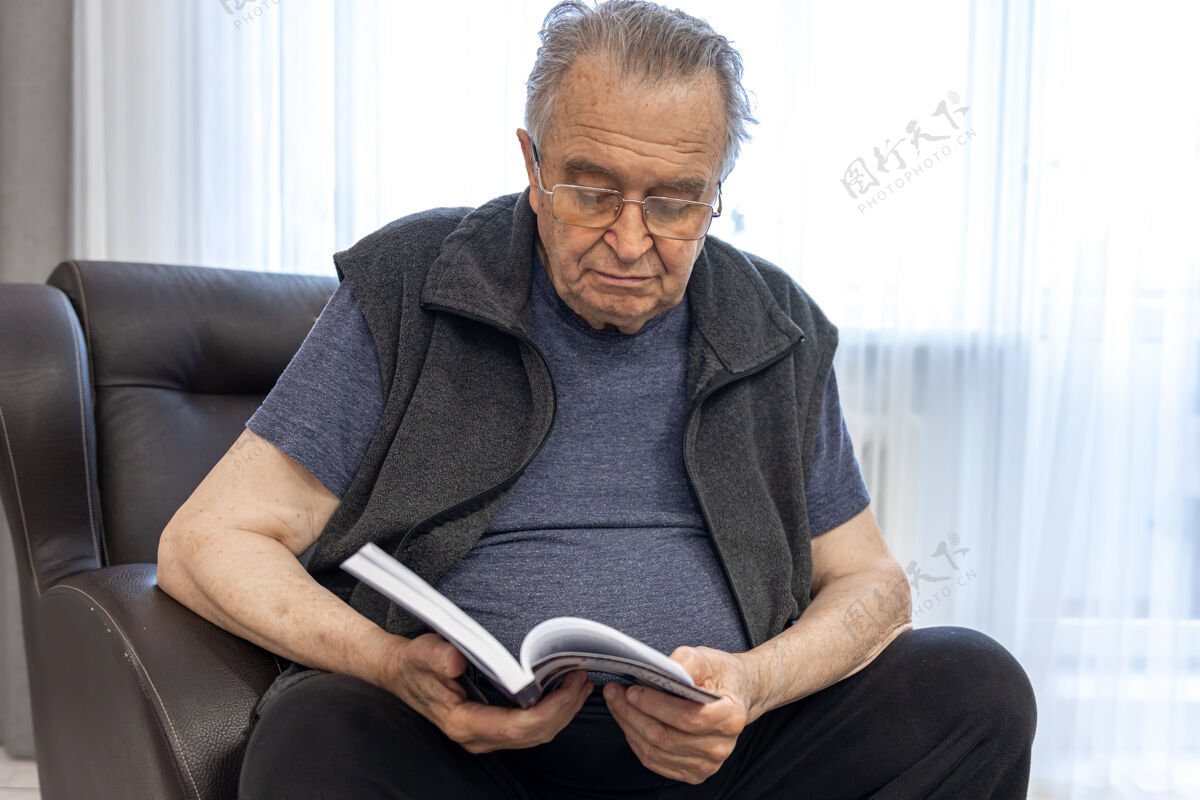 养老一位戴眼镜的老人坐在扶手椅上看书祖父坐着家具