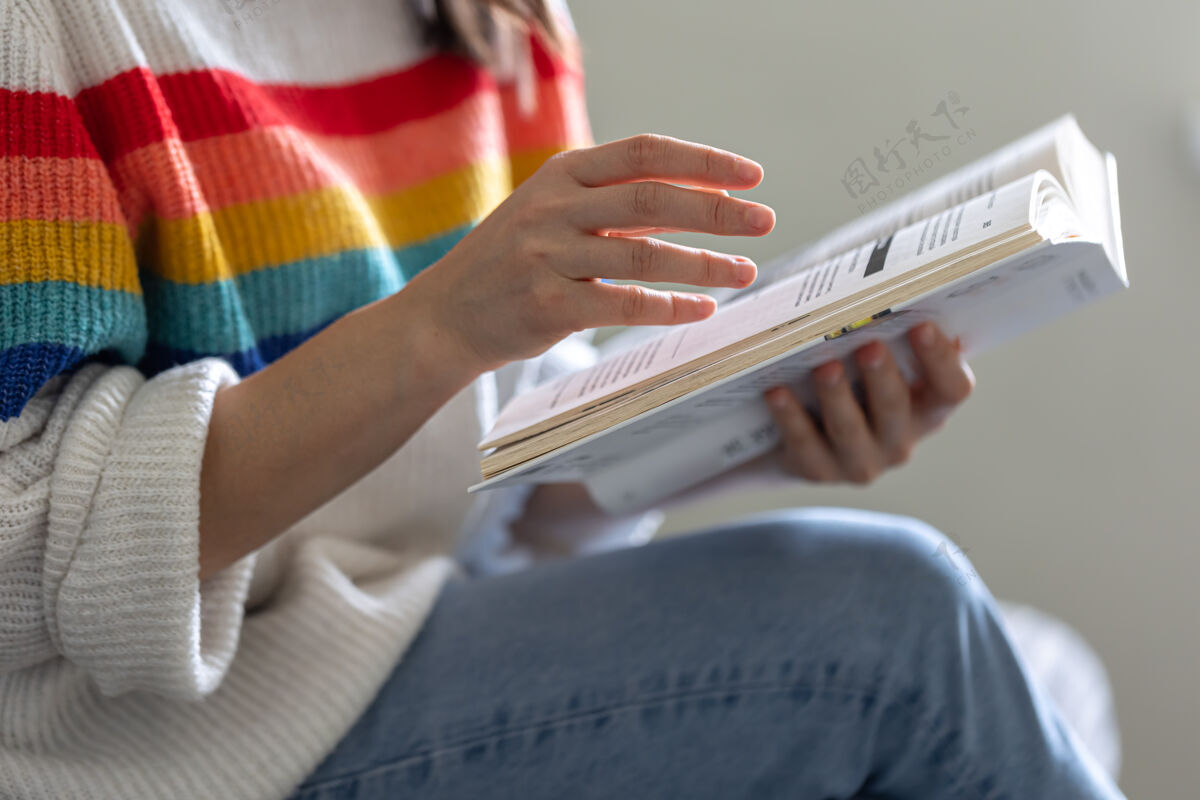 生活一个穿着鲜艳毛衣的女孩手里拿着一本打开的书的特写镜头文学华丽沙发