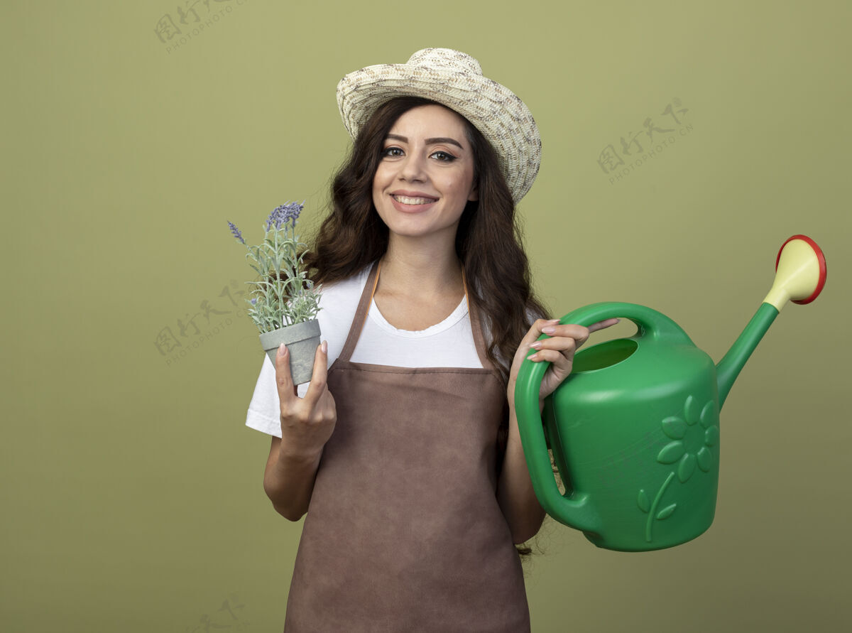 花园身着制服 戴着园艺帽 面带微笑的年轻女园丁 手拿浇灌罐 把花盆孤立在橄榄绿的墙上人园艺制服