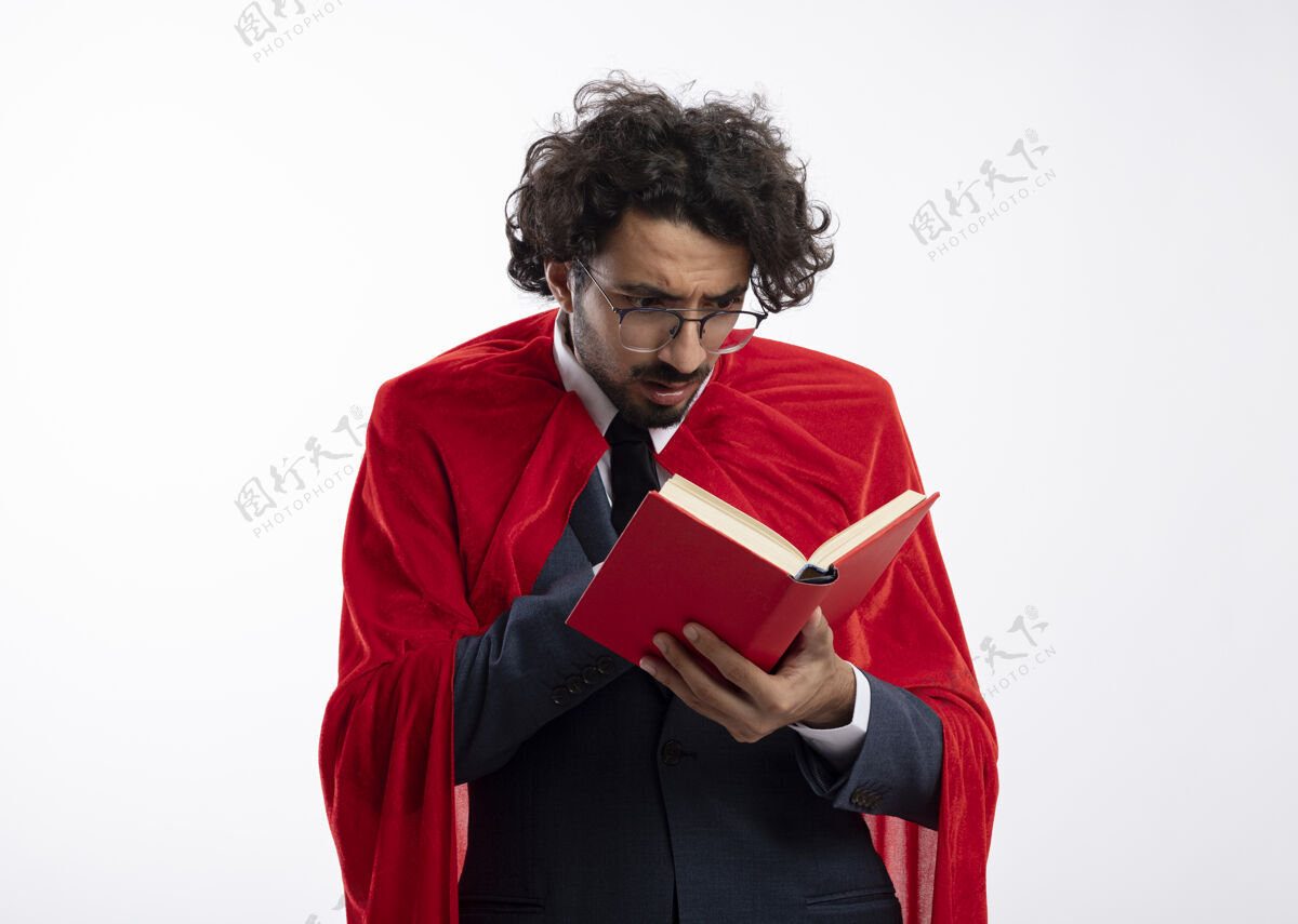 脸震惊的年轻超级英雄戴着眼镜 穿着红色斗篷的西装 拿着书 看着隔离在白墙上的书人穿着公民