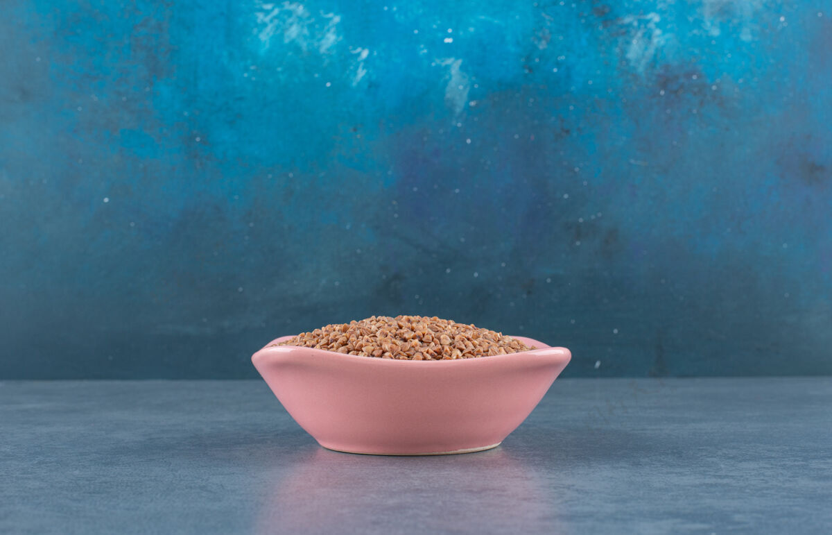 谷物荞麦堆在一个粉红色的碗里 堆在蓝色的地上生的谷类烹饪