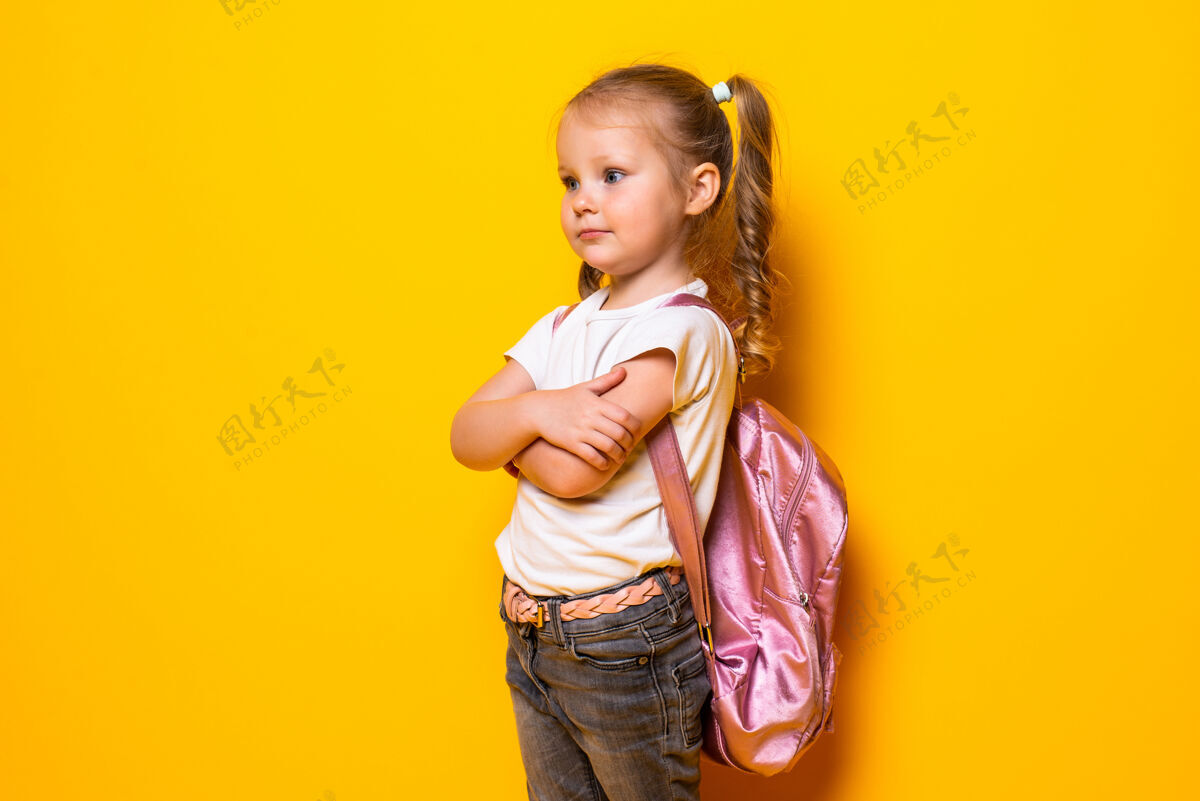 快乐黄色墙上一个带着背包微笑的小女生的画像孩子辫子女孩