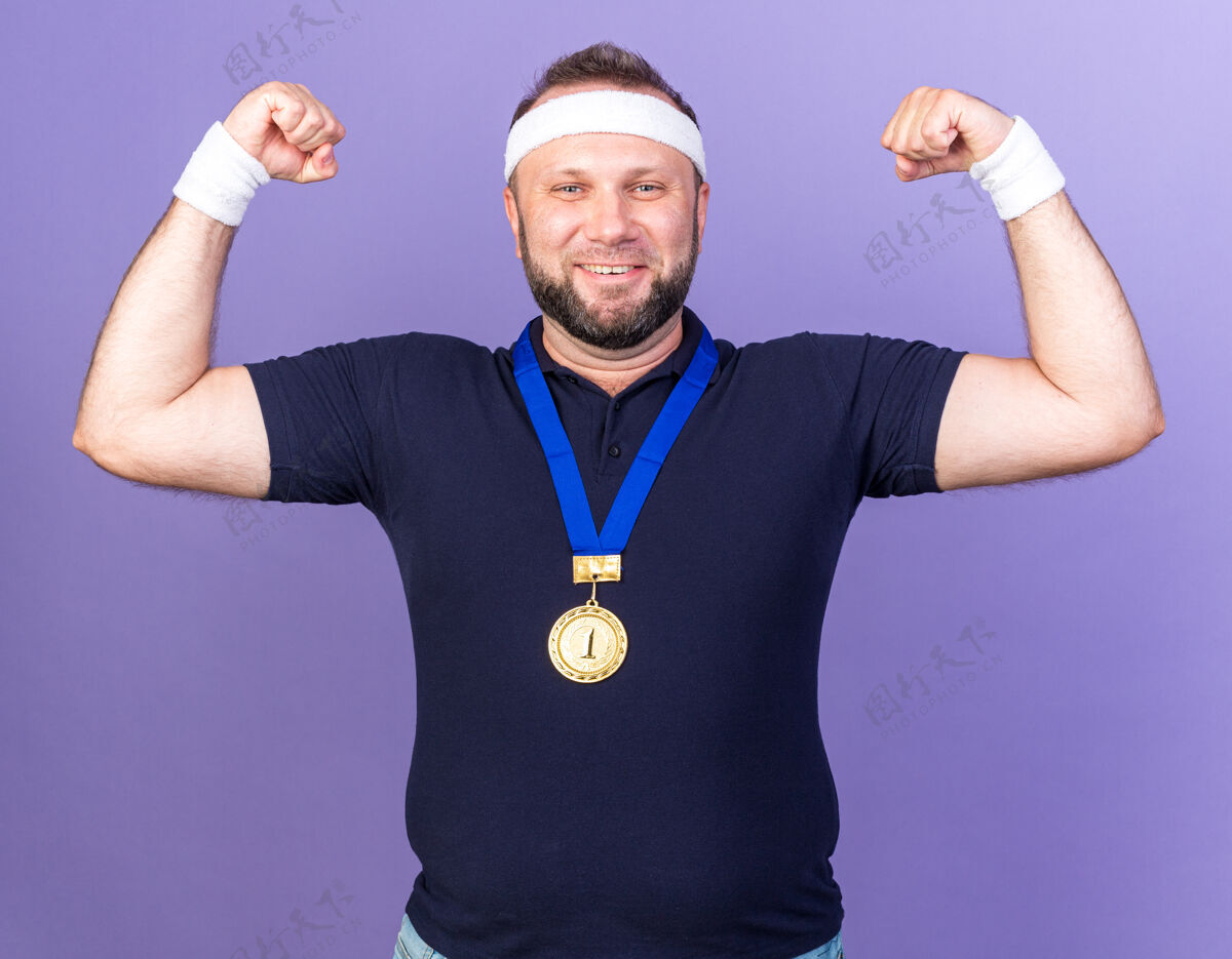 成人微笑的成年斯拉夫运动男子脖子上戴着金牌戴着头带和腕带紧张的肱二头肌隔离在紫色墙上复制空间周围斯拉夫头带