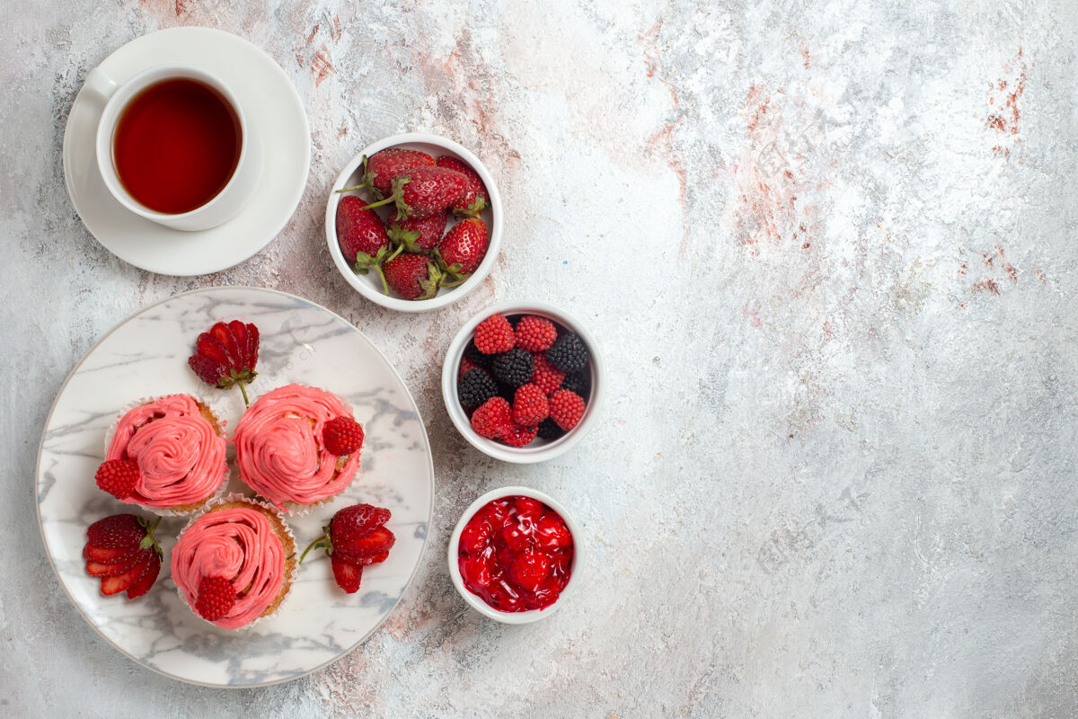 糖粉红色草莓蛋糕的顶视图 白色表面上有一杯茶饼干浆果茶