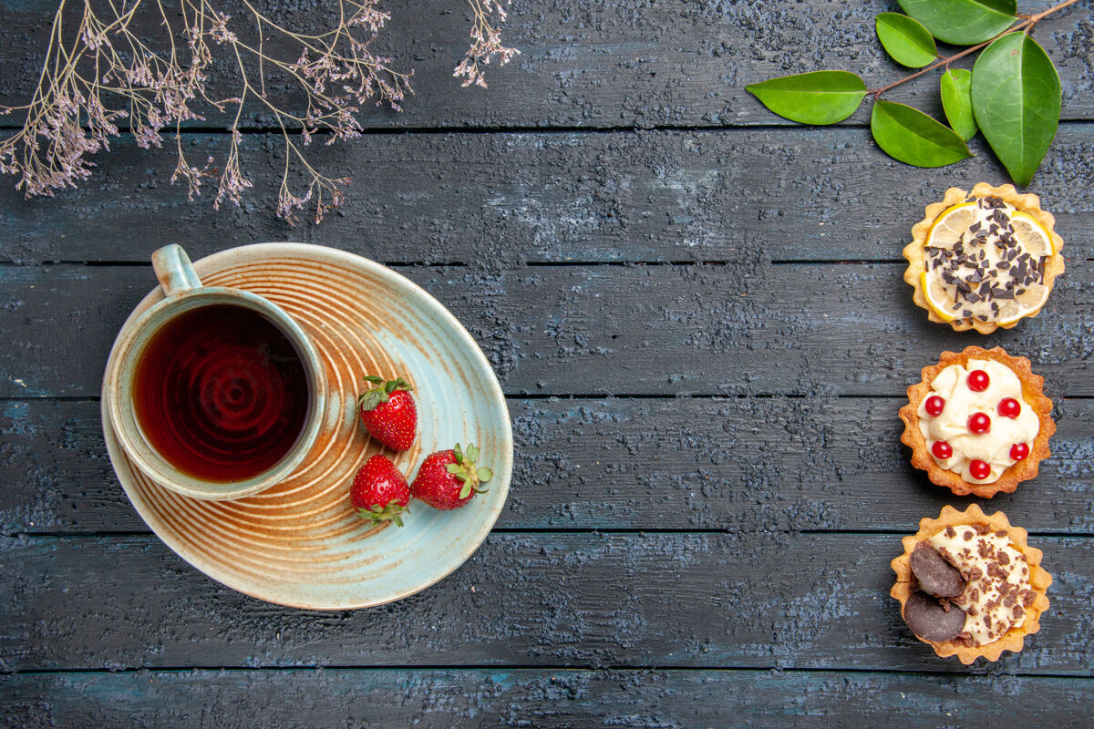 垃圾俯视图茶碟上的一杯茶和草莓在左边的馅饼叶在右边的深色木桌上食物茶深色
