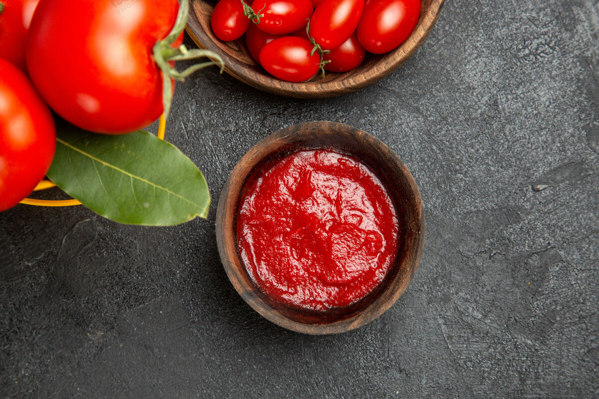 食品顶视图一桶西红柿和月桂叶碗樱桃西红柿和番茄酱在黑暗的地面上健康可食用水果樱桃