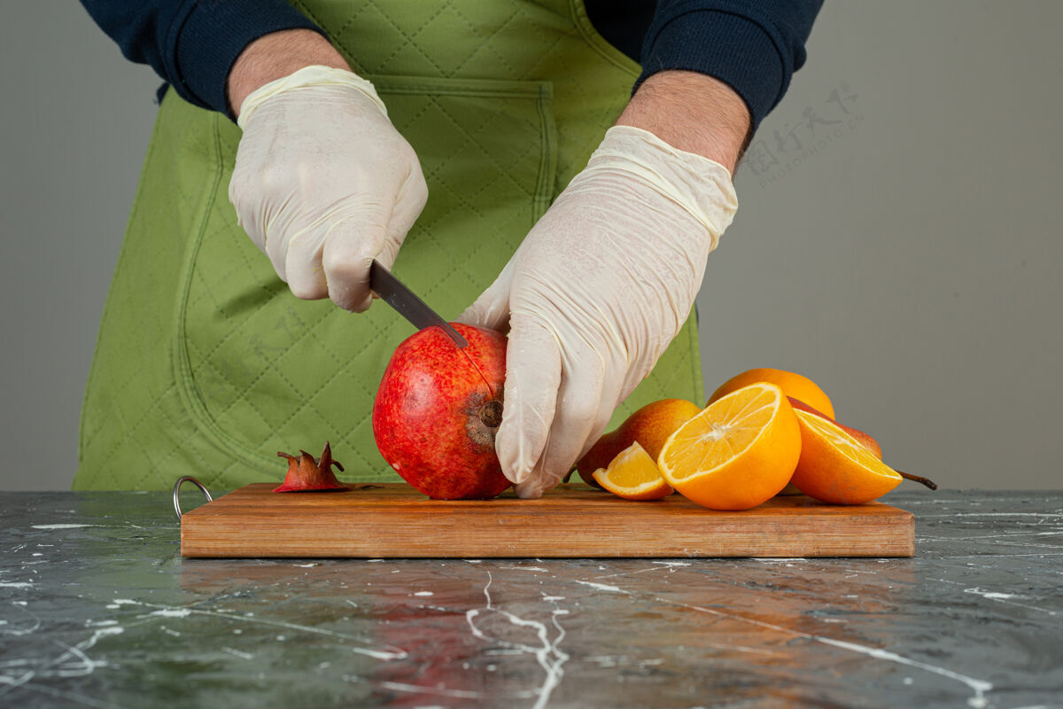 手套男手切新鲜石榴放在桌上的木板上水果手橙子