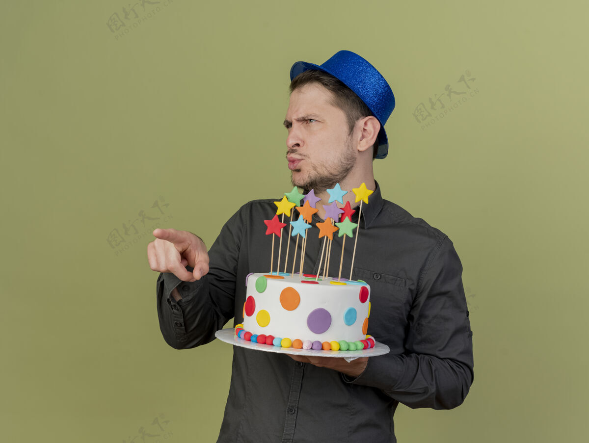 派对令人印象深刻的年轻人穿着黑色衬衫和蓝色帽子拿着蛋糕 并在橄榄绿孤立的一边点蓝色点橄榄