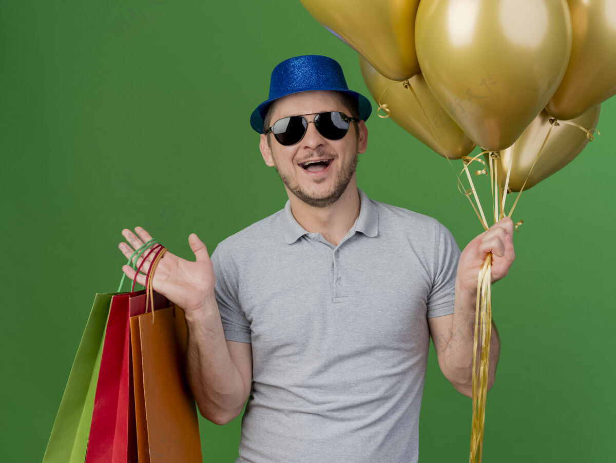 绿色快乐的年轻人戴着聚会帽 戴着眼镜 手里拿着一个礼品袋 绿色的气球被隔离开来包年轻人帽子