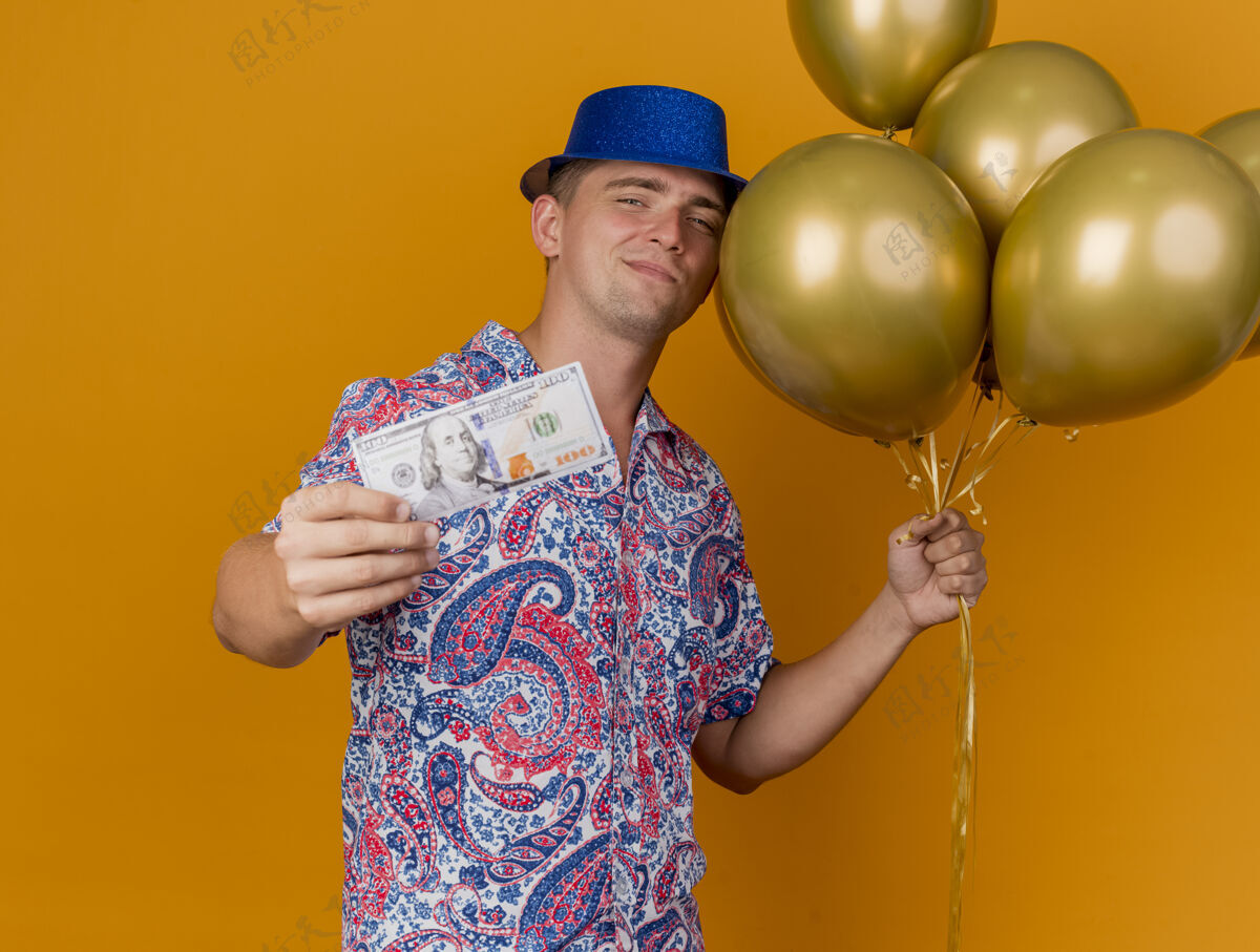 年轻人高兴的年轻人戴着蓝帽子 拿着气球 拿着现金孤立在橙色小伙子请拿着橙色