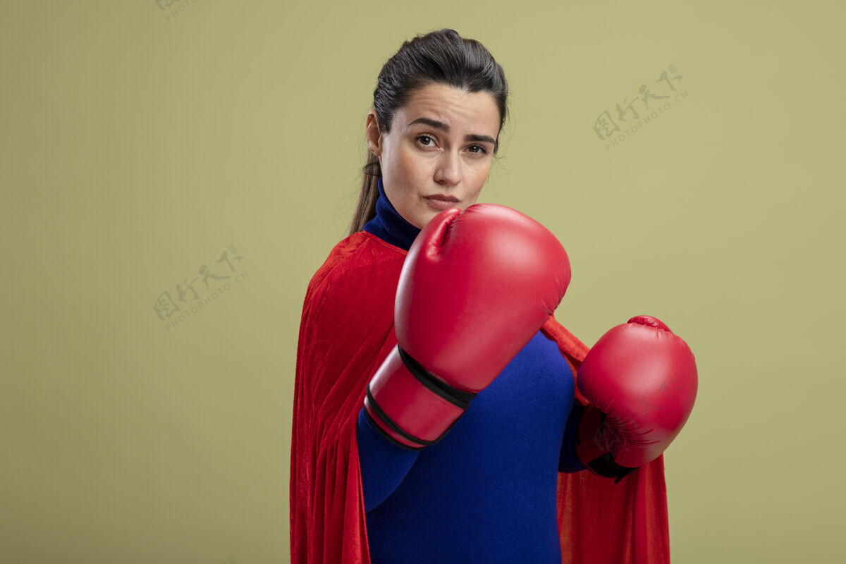 年轻自信的年轻超级英雄女孩戴着拳击手套站在橄榄绿的孤立无援的战斗姿势手套拳击绿色