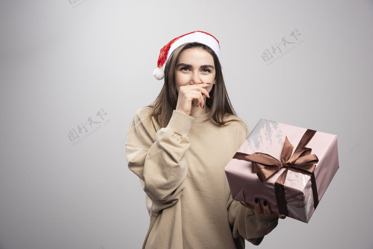漂亮在灰色背景下拿着圣诞礼物的年轻女子女性圣诞节表情
