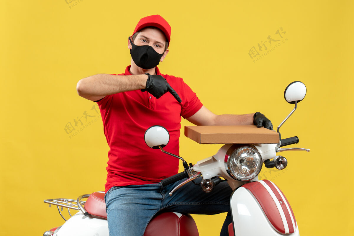 男子俯视图：骄傲自信的快递员身穿红色上衣 戴着帽子手套 戴着医用面罩 坐在滑板车上显示秩序体育摩托车球