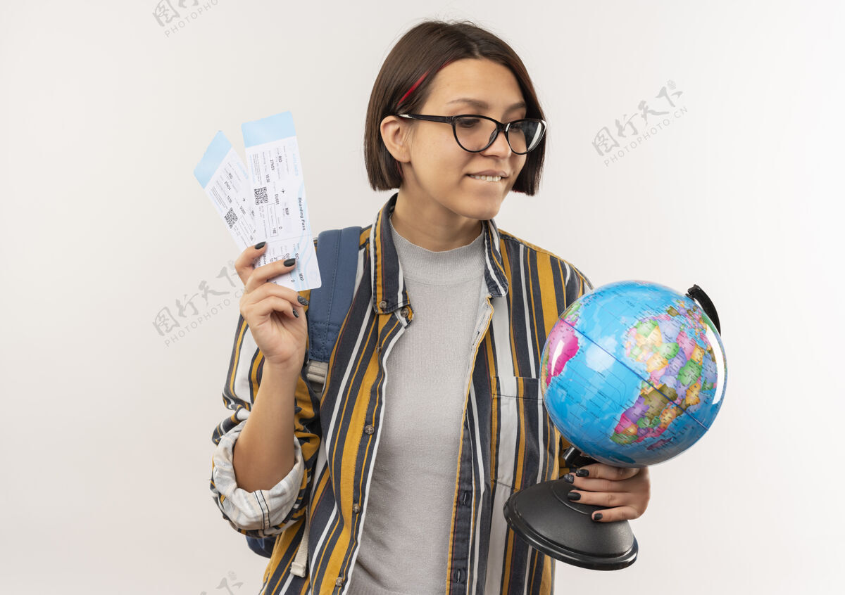 公民高兴的年轻学生女孩戴着眼镜 背着包拿着飞机票和地球仪看着隔离在白墙上的地球仪表情女孩白色