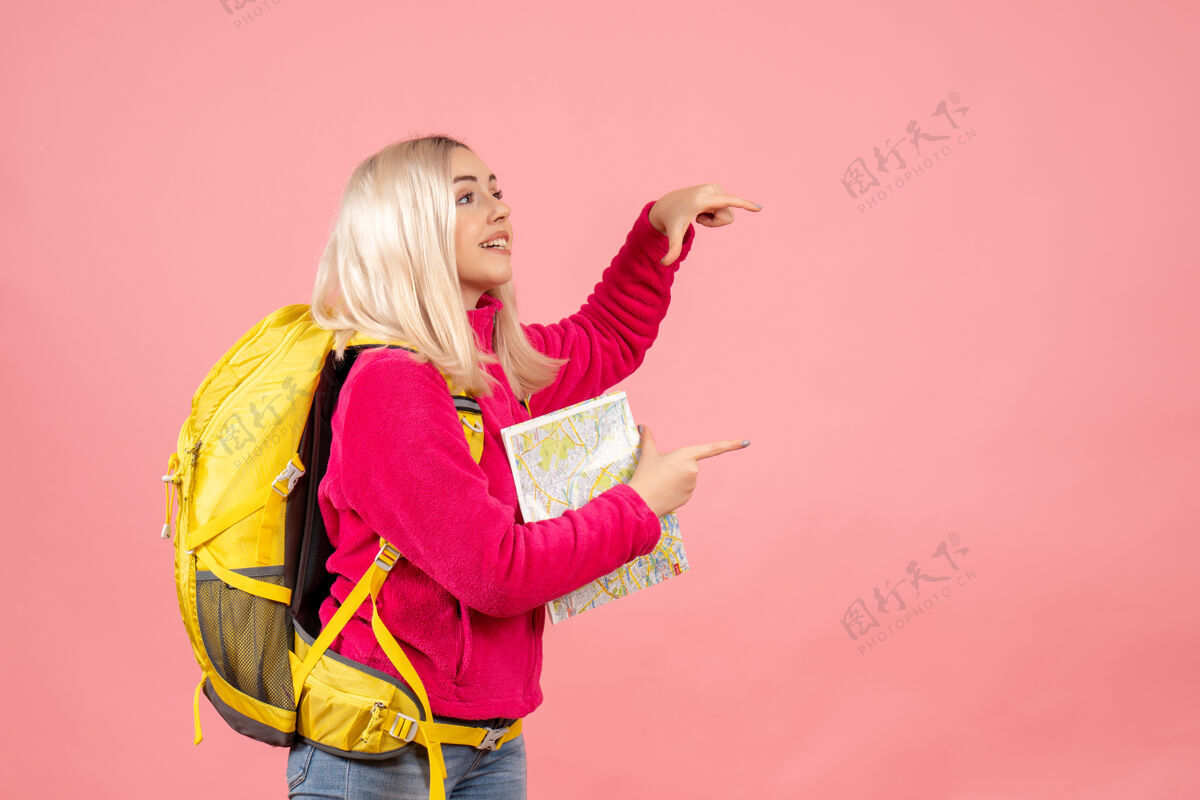 女旅客正面是一个旅行妇女 背着黄色的背包 在粉色的墙上拿着地图成人持有地图